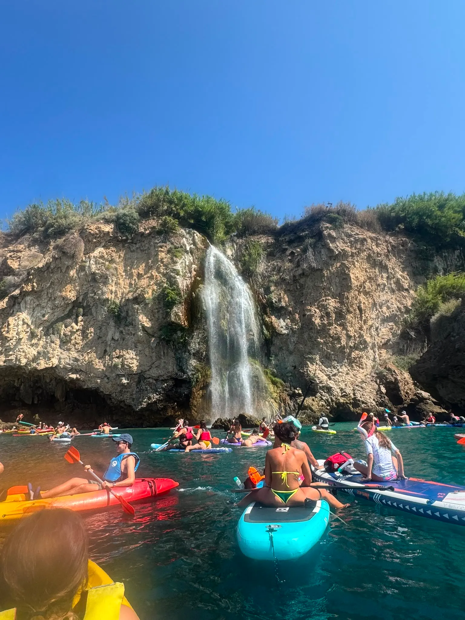 Kayaks and paddleboards gathered in the cove beneath the Maro waterfall on a busy July morning